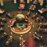 High-angle view of a library interior featuring a central globe and wooden tables, symbolizing knowledge and exploration.